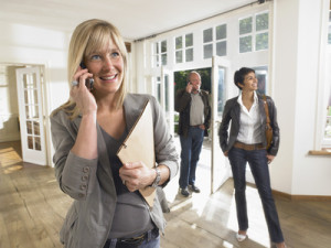 female real estate agent on phone in show house clients behind.